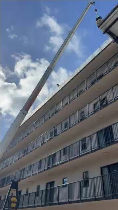 Commercial crane hoisting a central air conditioner condenser unit onto the roof of a multi-story Naples condo complex during an installation by Elevate Home Services.